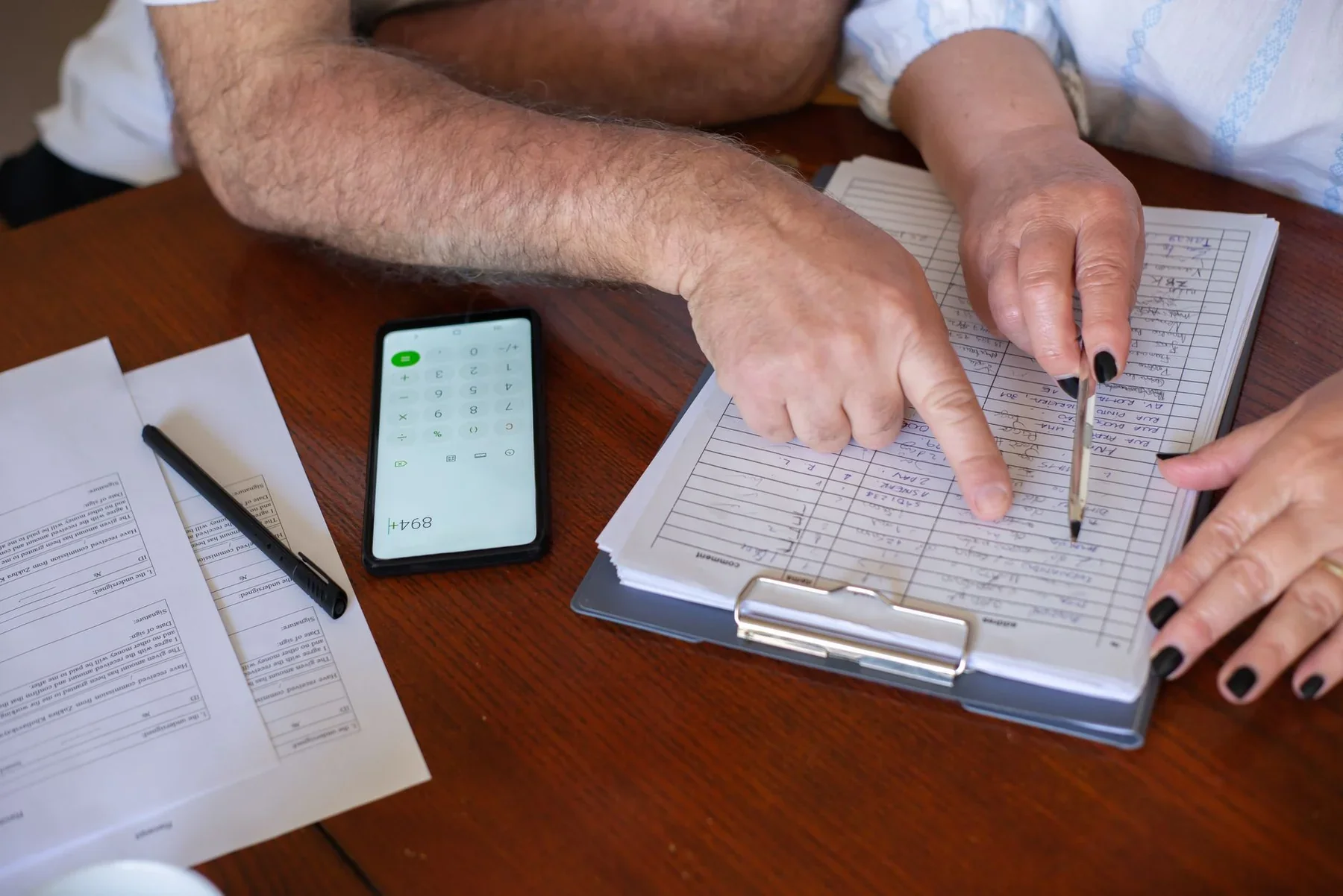People at a table reviewing bills, a calculator, and a clipboard with handwritten notes.