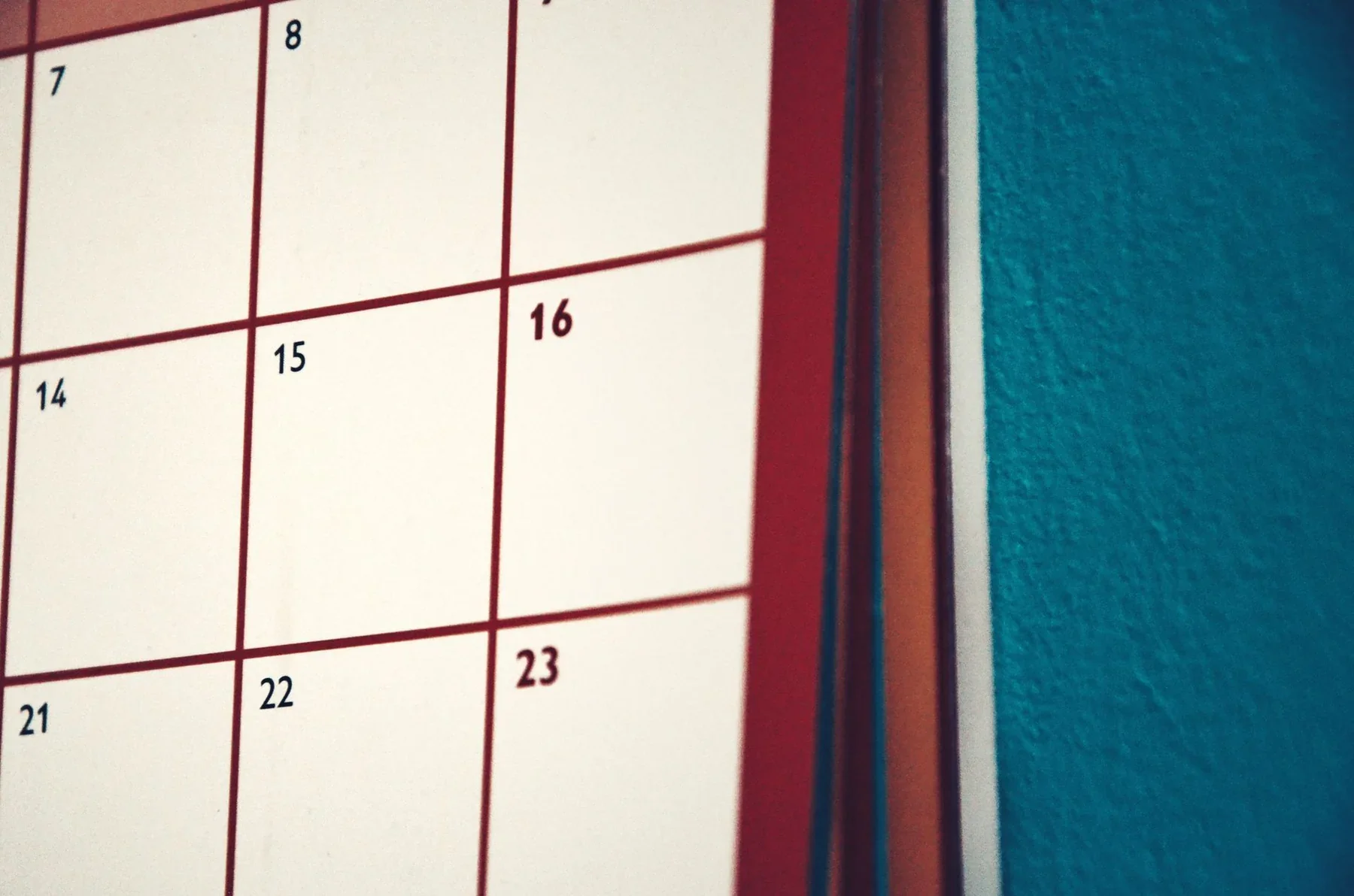 Close-up of a wall calendar with numbered date boxes beside a teal wall.